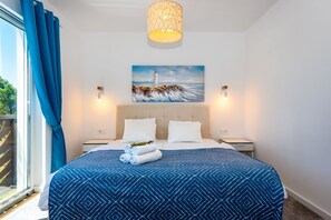 A hotel room with a large bed, a painting of a lighthouse, two bedside tables, and a window with curtains. - Villa Lemon Beach (Vodice)