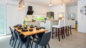 Een moderne keuken met een eethoek, met een houten tafel, zwarte stoelen en een bar met witte krukken.
