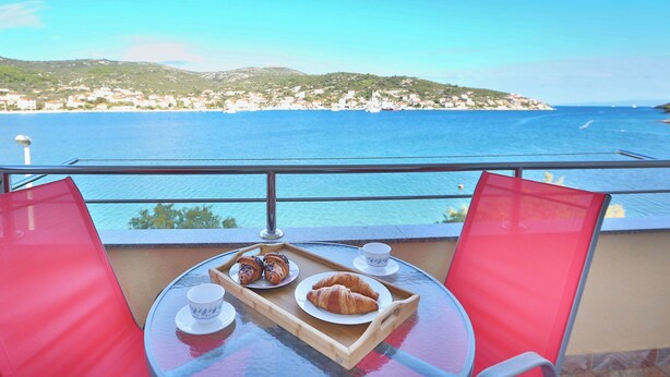 Un balcón con una mesa lista para el desayuno, con vistas a un pueblo costero y al mar.