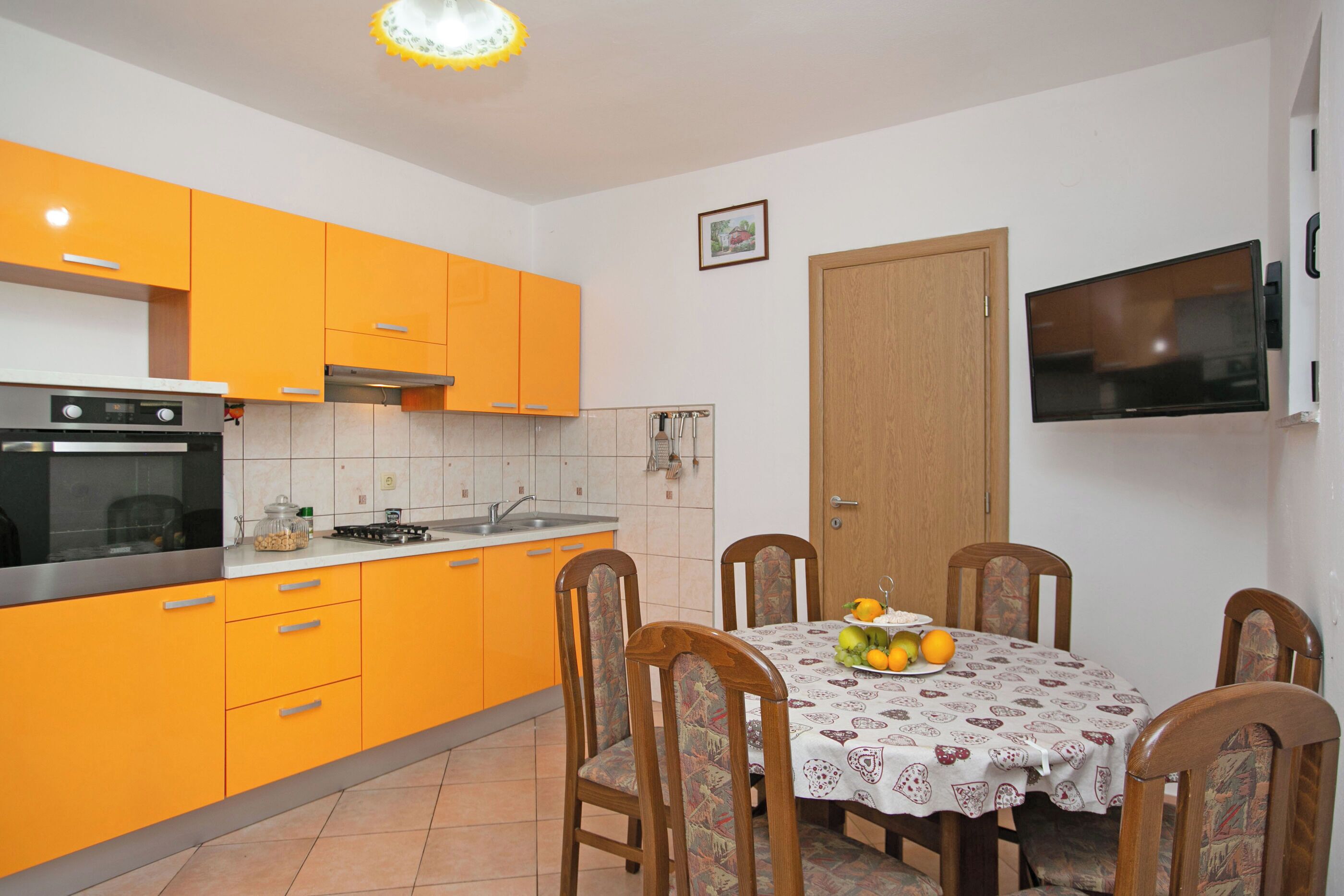 A kitchen with orange cabinets, a stove, and a dining table with chairs.