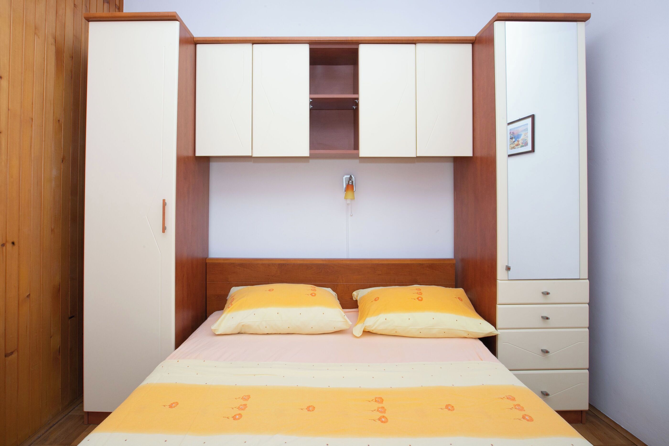 Un dormitorio con una cama, dos almohadas, cabecera de madera, un armario y un mueble pequeño.