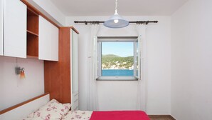 Un dormitorio con cama, ventana con vista a la playa y un armario de madera.