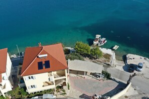 A coastal building with a red-tiled roof, adjacent to a clear blue sea. - Apartments Tiho (Marina)