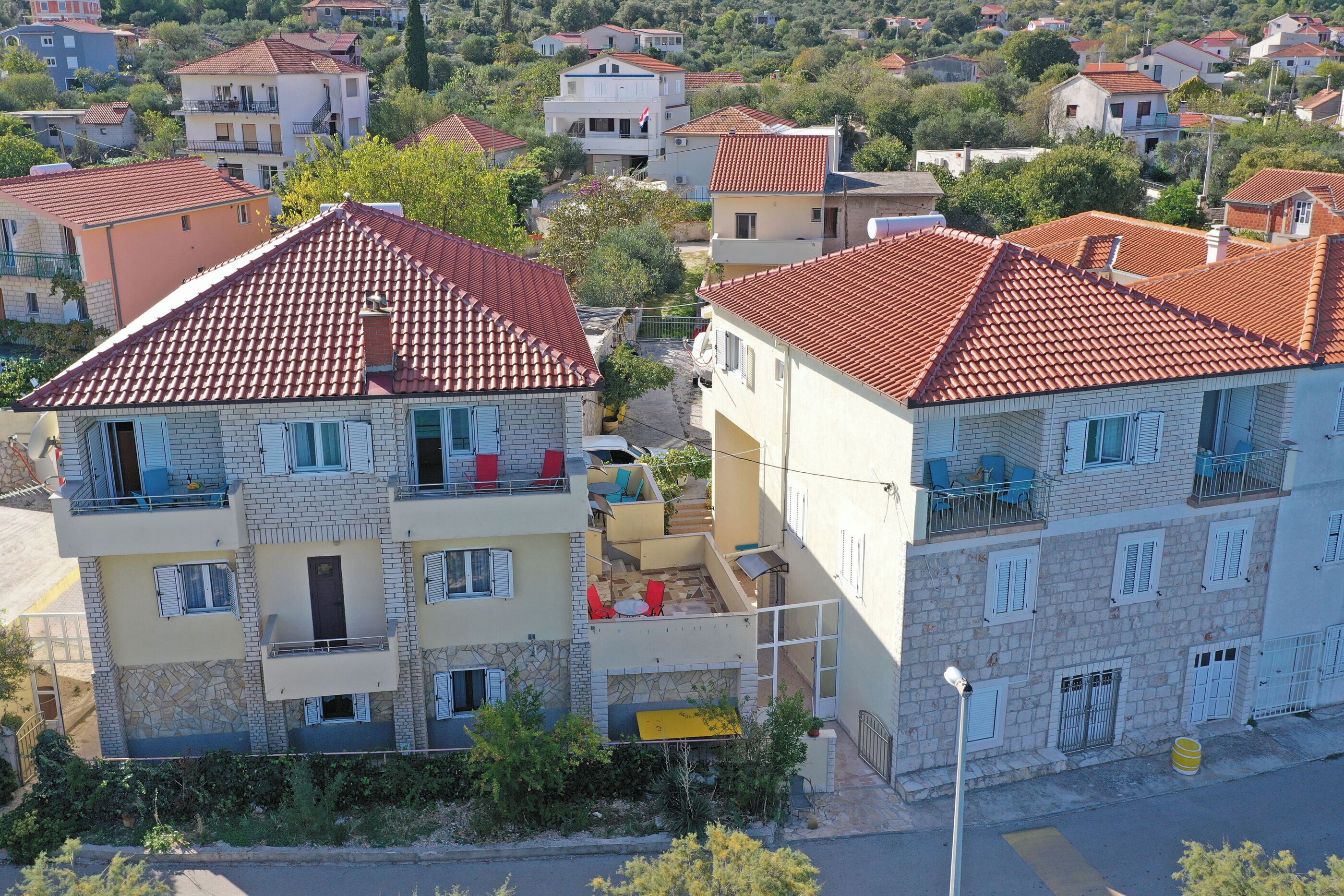 A multi-story residential building with a red-tiled roof, balconies, and a small outdoor seating area.