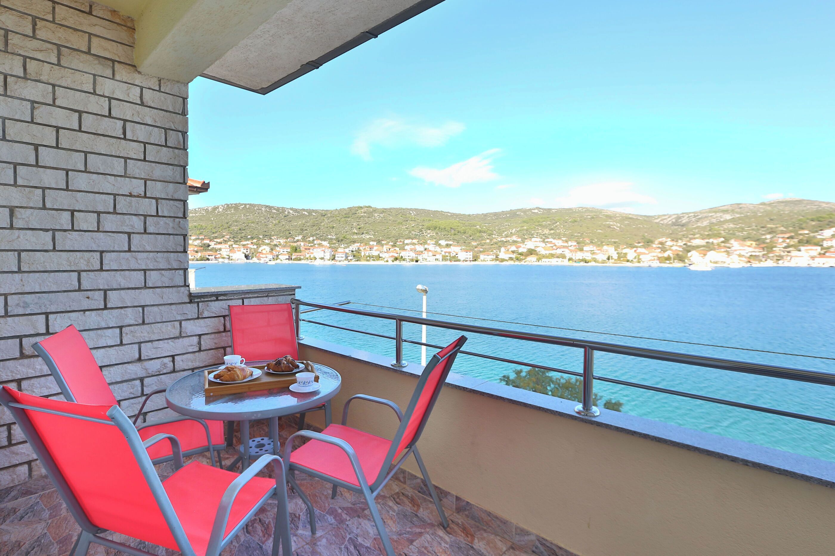 Ein Balkon mit Tisch und Stühlen mit Blick auf eine Küstenstadt und das Meer.