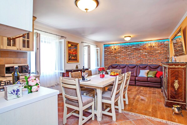 A dining area with a white table and chairs, a brick wall, and a brown leather sofa. - House Pelegrin (Vela Luka)