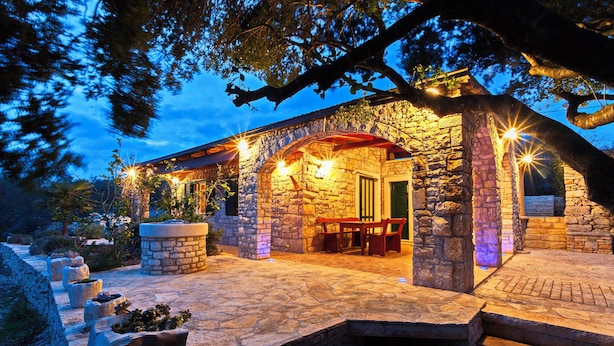 A stone building with a covered patio, outdoor seating, and stone planters. - House Pelegrin (Vela Luka)