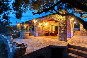 A stone building with a covered patio, outdoor seating, and stone planters. - House Pelegrin (Vela Luka)