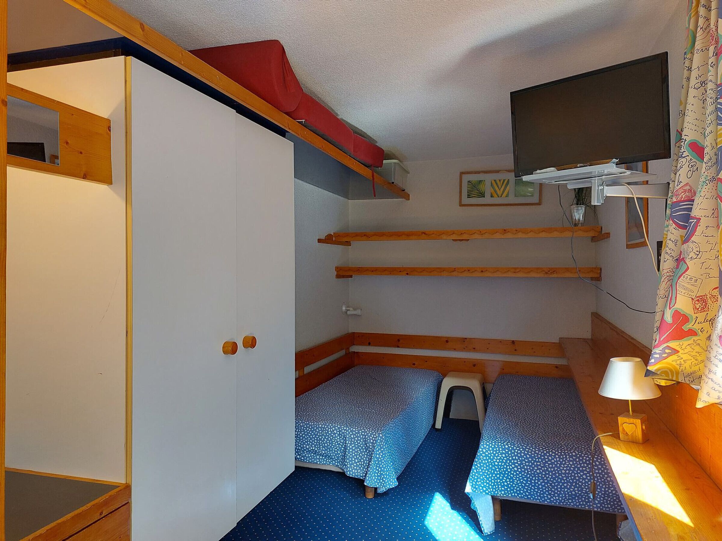 A compact room with bunk beds, a small stool, a TV, and a window with a curtain.