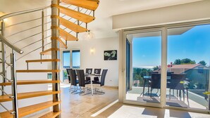 Ein modernes Interieur mit Wendeltreppe, Essbereich und einem Balkon mit Aussicht.