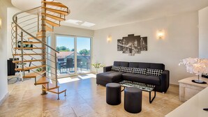 Ein modernes Wohnzimmer mit einer Wendeltreppe, einem schwarzen modularen Sofa und einer Glastür, die zu einem Außenbereich führt.