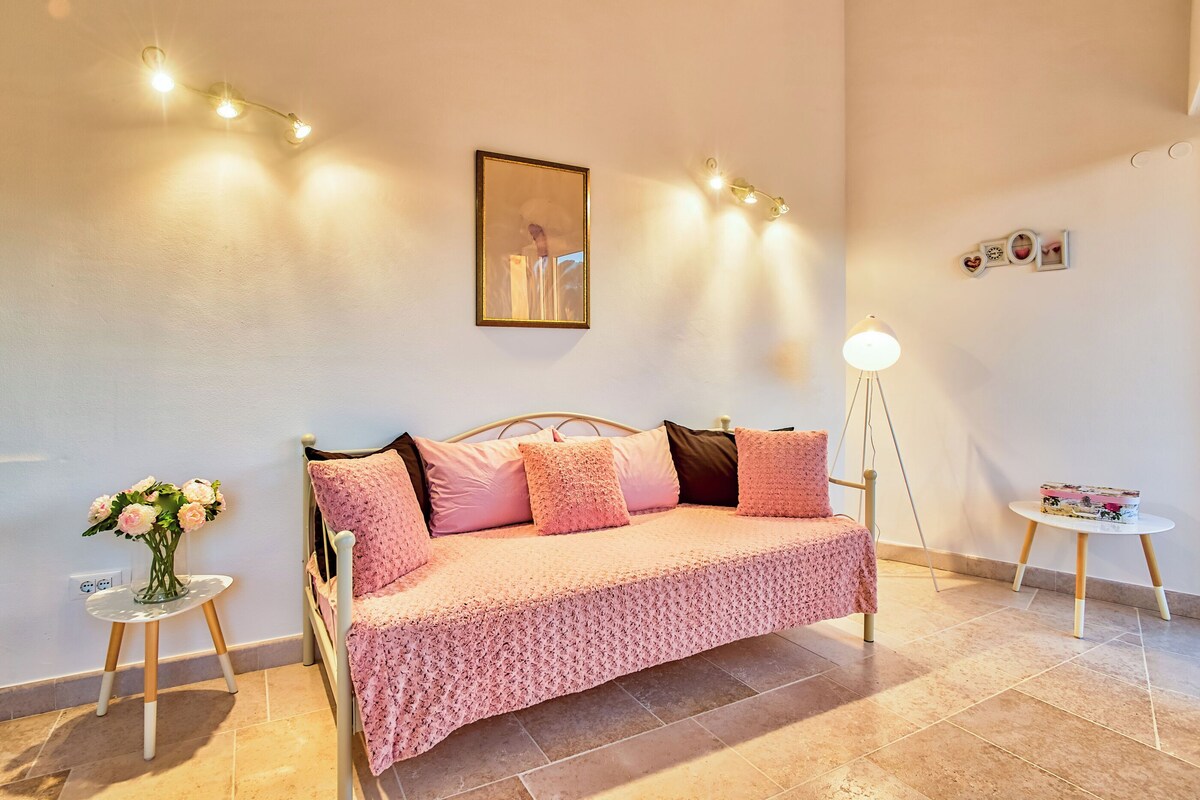 A bedroom with a bed, a bedside table with a vase of flowers, a lamp, and wall-mounted lights.