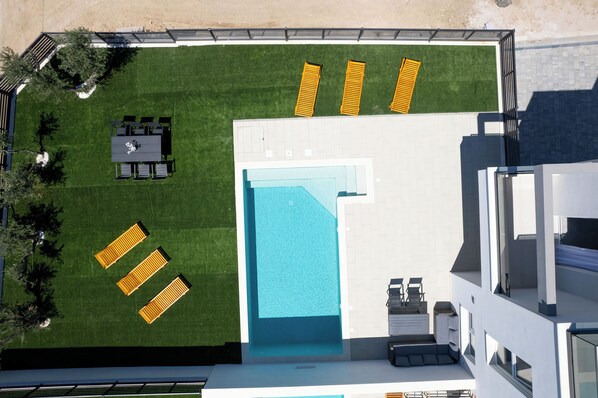 An aerial view of a modern building with a swimming pool, outdoor seating, and a well-maintained lawn. - Villa Flora (Kastela)