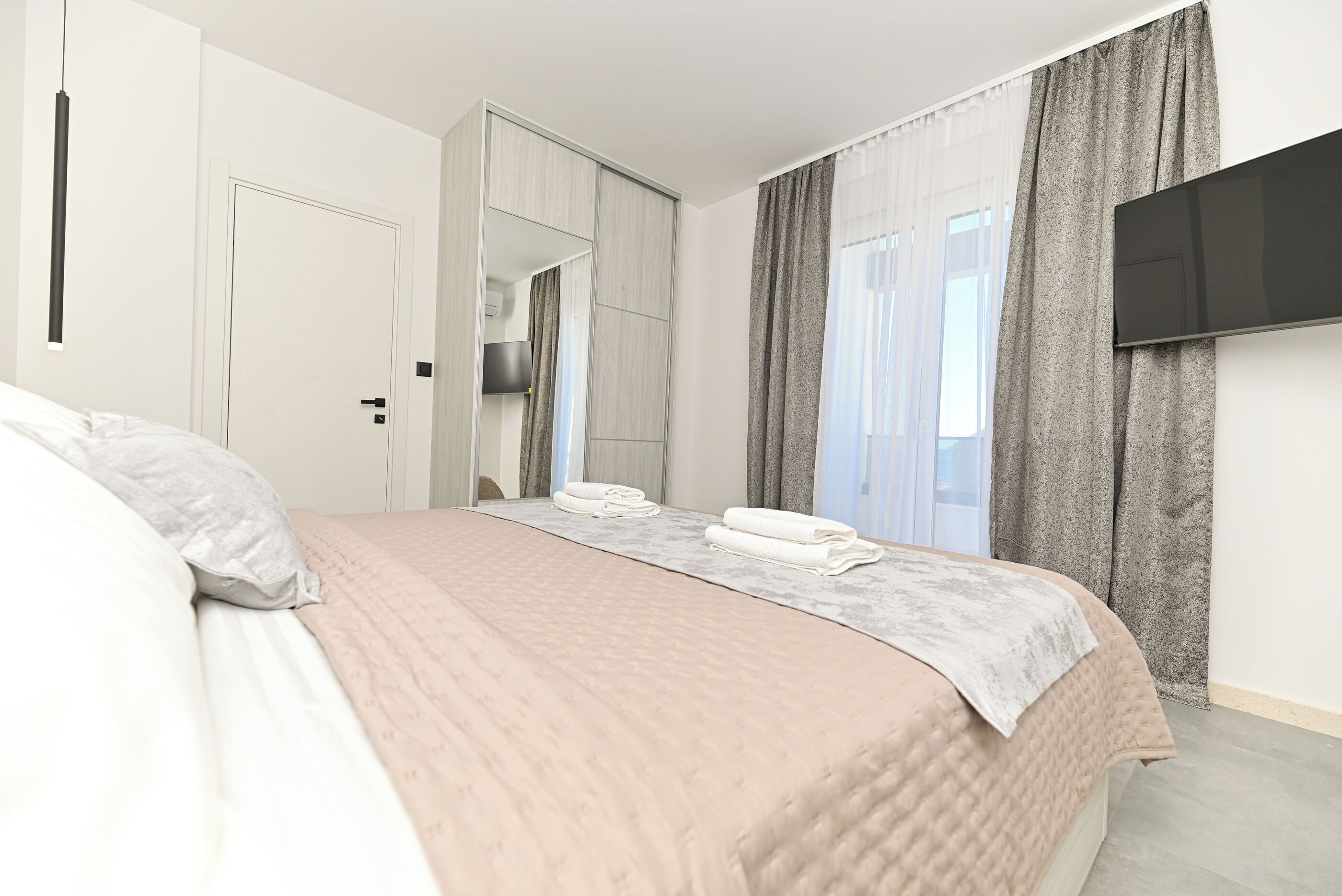 Habitación de hotel con cama, armario, televisor de pantalla plana y ventana con cortinas.