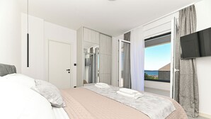 A modern bedroom with a large bed, a walk-in closet, a bathroom, and a balcony with a TV. - Villa Flora (Kastela)