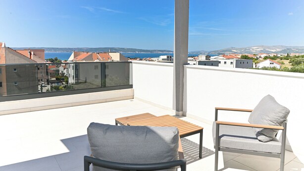 A balcony with a view of the sea and buildings, a wooden table, and two chairs. - Villa Flora (Kastela)