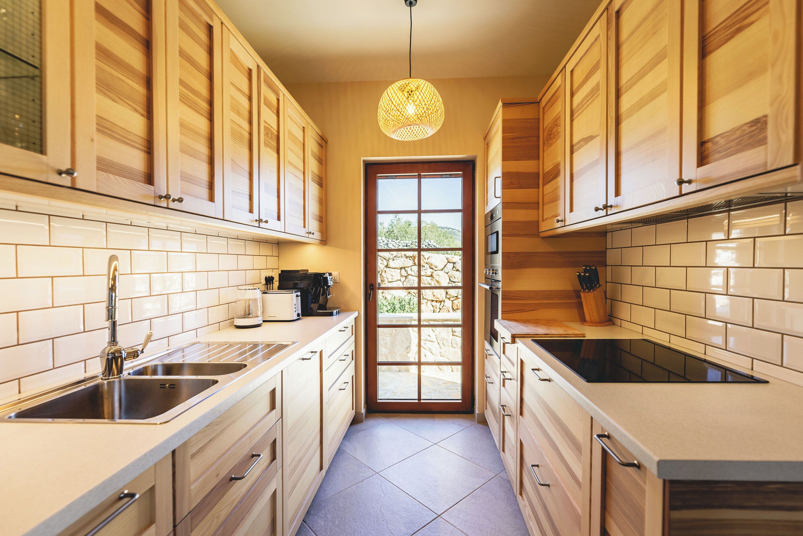 A narrow kitchen with wooden cabinets, a double sink, and a large window.