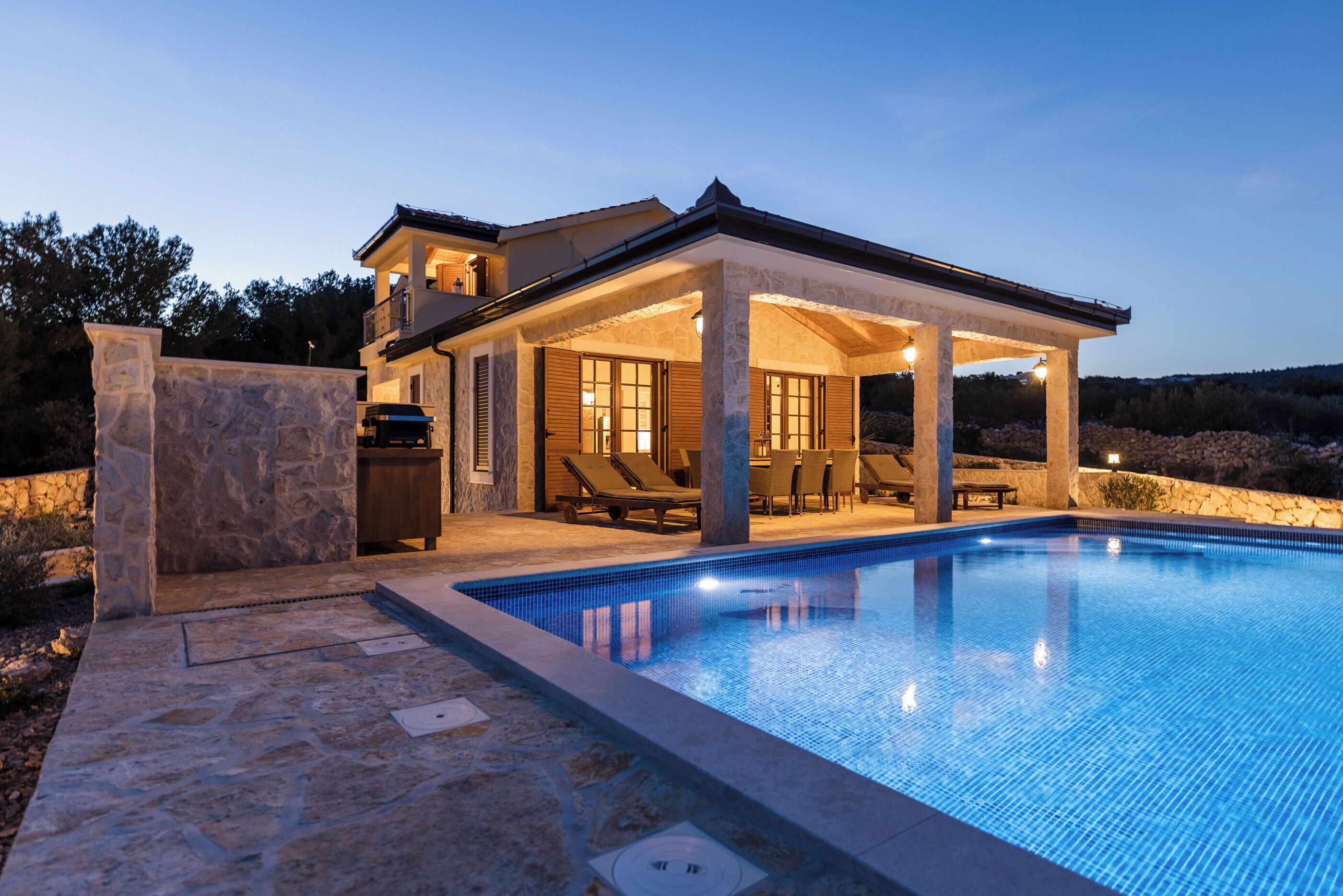 A two-story house with a swimming pool, stone walls, and outdoor seating.