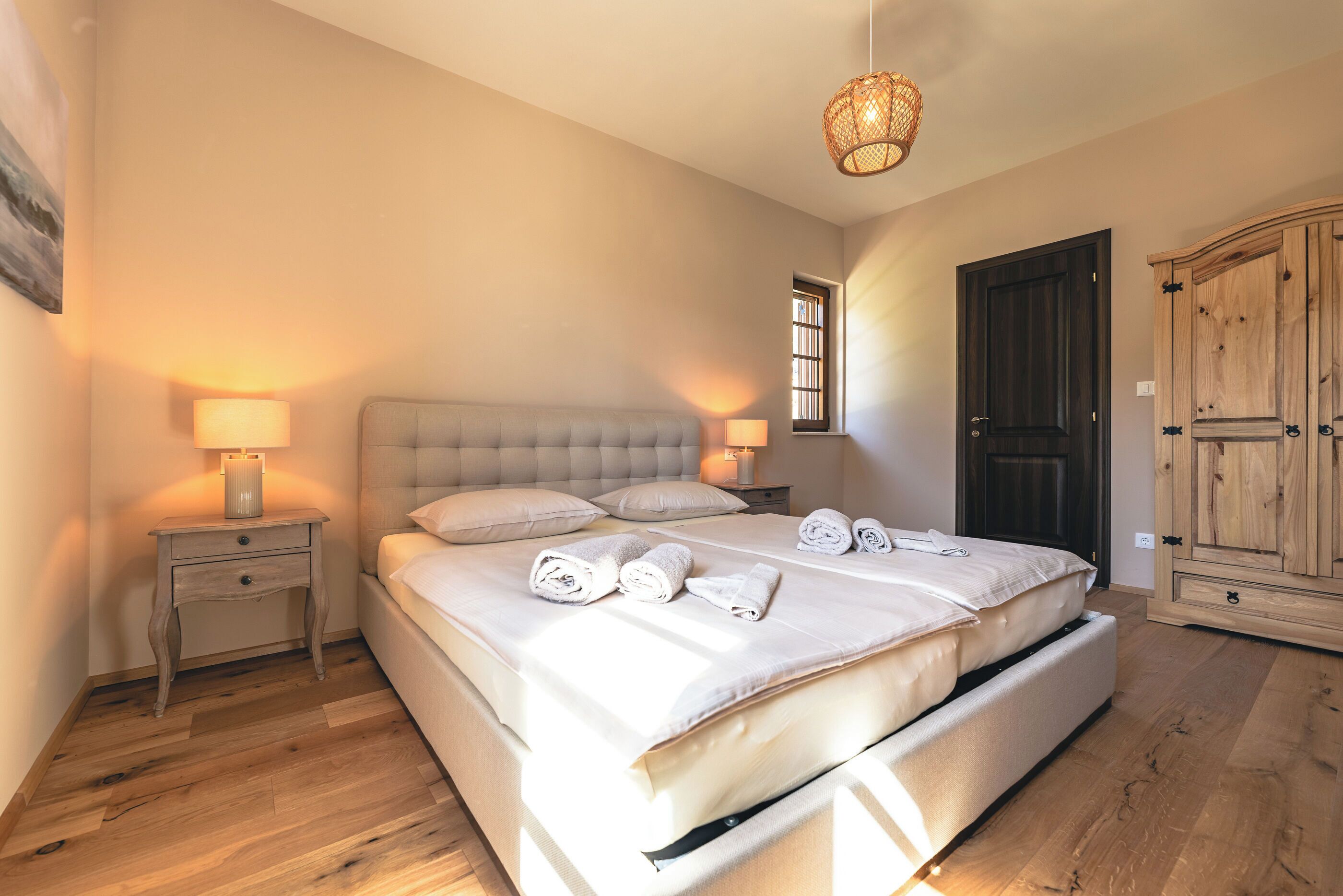 Un dormitorio con una cama grande, dos mesitas de noche con lámparas, un armario de madera y una ventana.