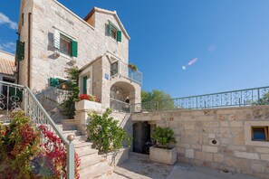 Ένα κτίριο από πέτρα με μπαλκόνι, σκάλα και φυτά σε γλάστρες.