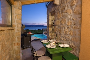 Un área de comedor al aire libre con vista a un lago y montañas, paredes de piedra y una piscina.