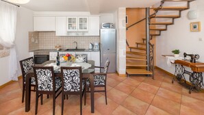 A compact kitchen with white cabinets, a refrigerator, and a dining area with patterned chairs. A spiral staircase leads to an upper level. - Villa Mare (Bol)