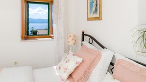 A bedroom with a bed, a window with a view, a lamp, and a painting on the wall. - Villa Mare (Bol)
