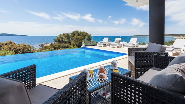Un espace aménagé au bord de la piscine, avec des chaises longues, une table où sont servis les articles du petit-déjeuner et une vue sur la mer.