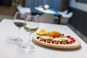 Une table avec deux verres à vin, l’un contenant du vin rouge et l’autre du vin blanc, ainsi qu’une planche en bois sur laquelle on trouve du fromage, des tomates et un croissant.