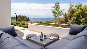 Un balcon avec un canapé et une table, offrant une vue panoramique sur la mer et la verdure.