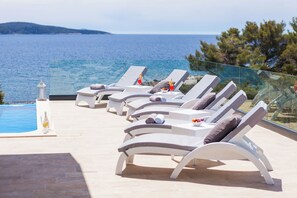 Un espace aménagé au bord de la piscine, avec des chaises longues et une rambarde en verre donnant sur la mer.