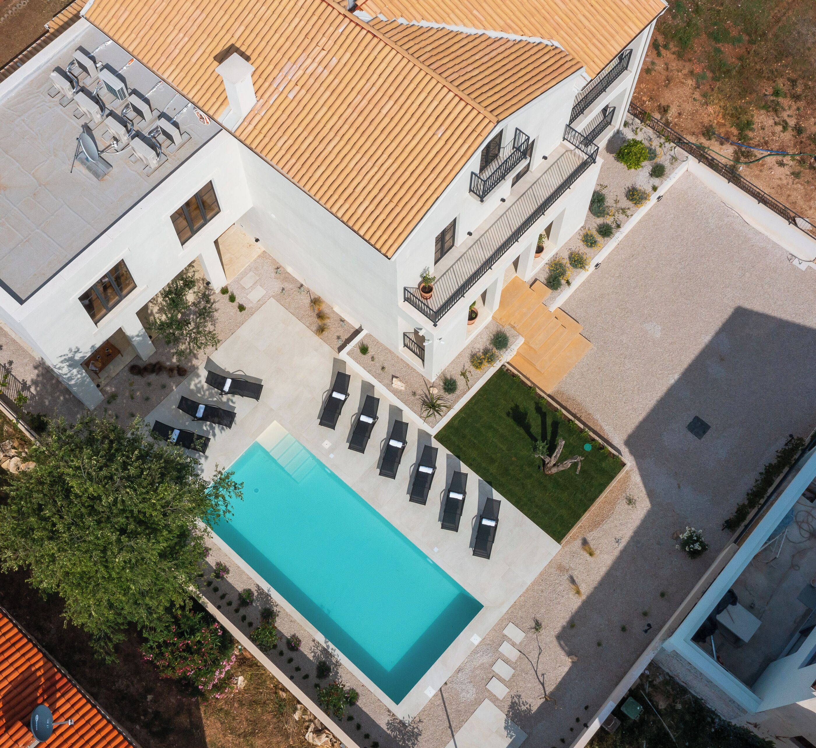 An aerial view of a modern building with a swimming pool, sun loungers, and a well-maintained garden.