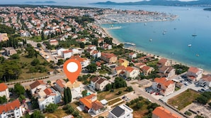 Vista aerea di una cittadina costiera con edifici residenziali, un porto turistico e una spiaggia.