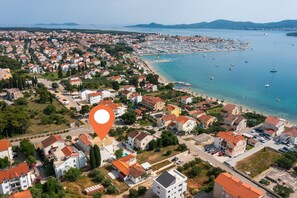 Eine Luftaufnahme einer Küstenstadt mit Wohnhäusern, einem Yachthafen und einem Strand.