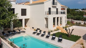 Una casa a due piani con piscina, area relax esterna e giardino.