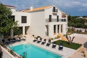 Ein zweistöckiges Haus mit Swimmingpool, Sitzgelegenheiten im Freien und einem Garten.