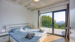 Ein Schlafzimmer mit Bett, Nachttischen, Blick durch eine Schiebetür und einer Decke mit sichtbaren Holzbalken.