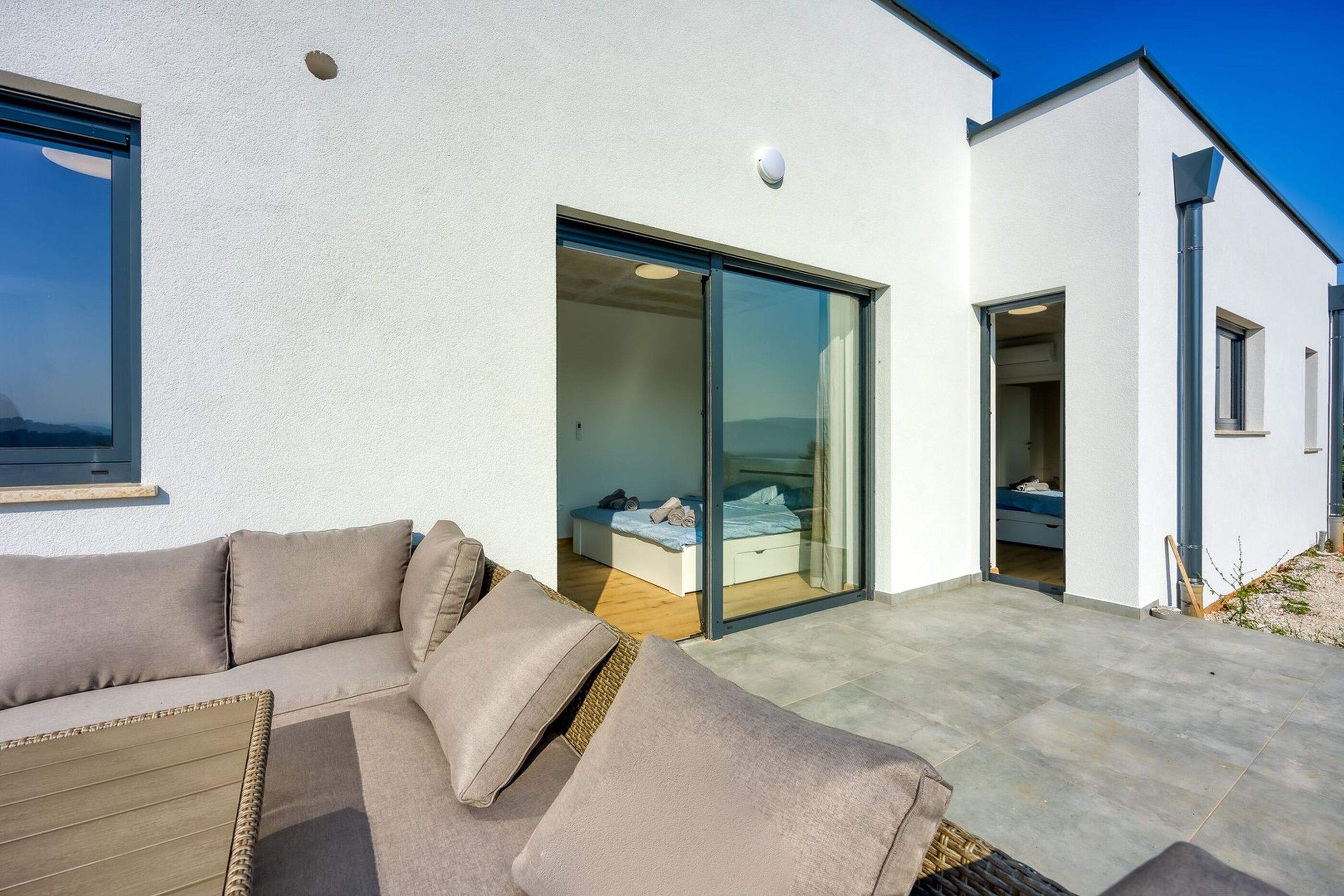 A modern building with a sliding glass door leading to a bedroom with a bed and a bench.