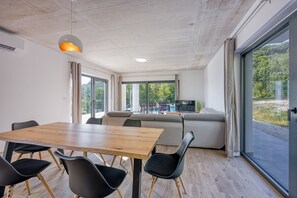 A modern interior with a wooden dining table, black chairs, a sofa, and a large window offering a view of outdoor furniture.