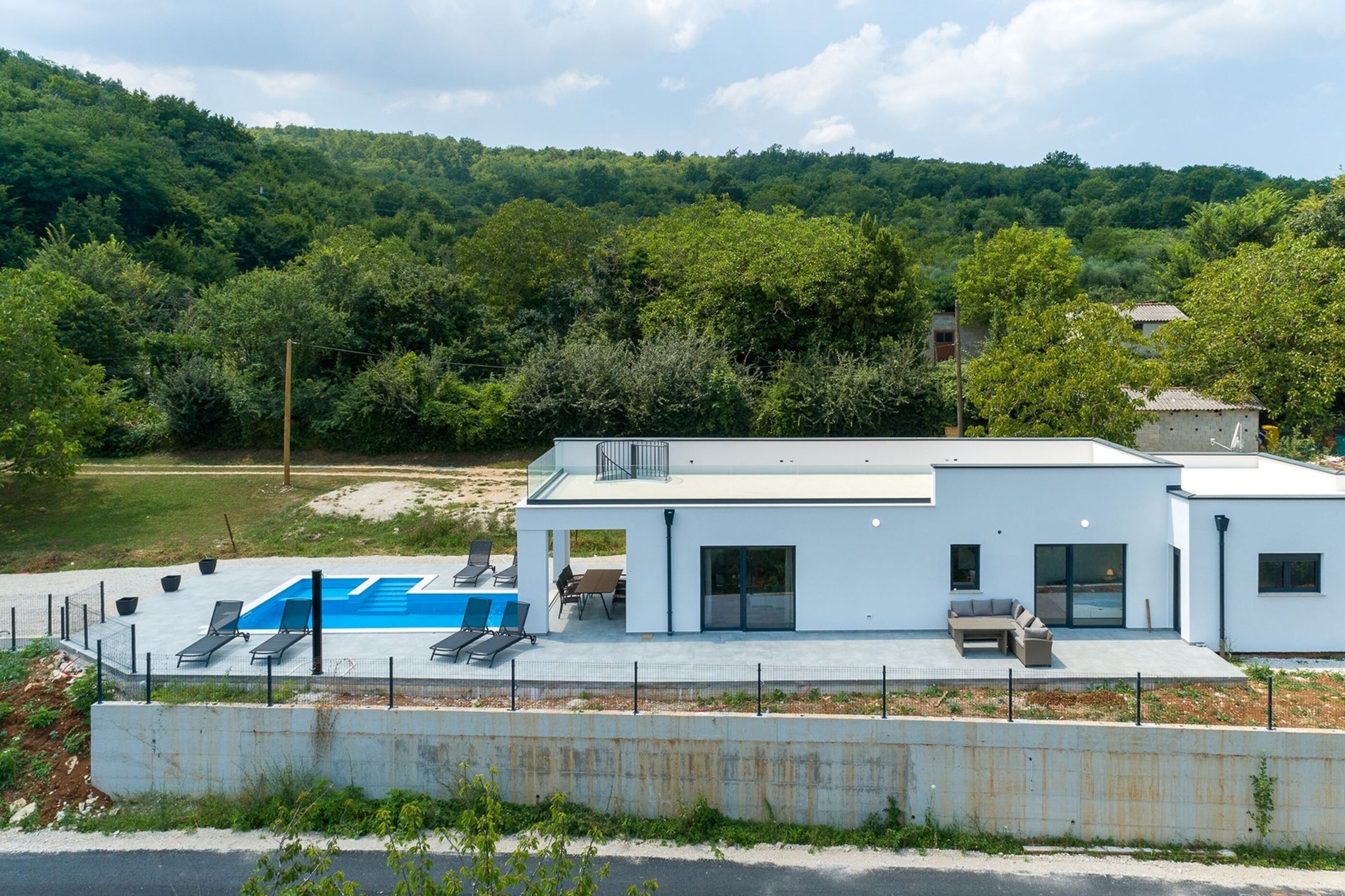 Et moderne hus med swimmingpool, balkon og udsigt til en skovklædt bakke.