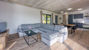 Ein modernes Wohnzimmer mit einer Eckcouch, einem Glastisch und einem Essbereich mit Holztisch und Stühlen.