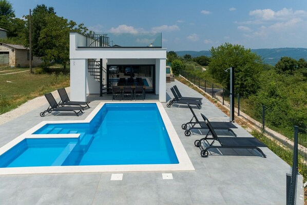 A modern house with a swimming pool, outdoor seating, and a view of the landscape.
