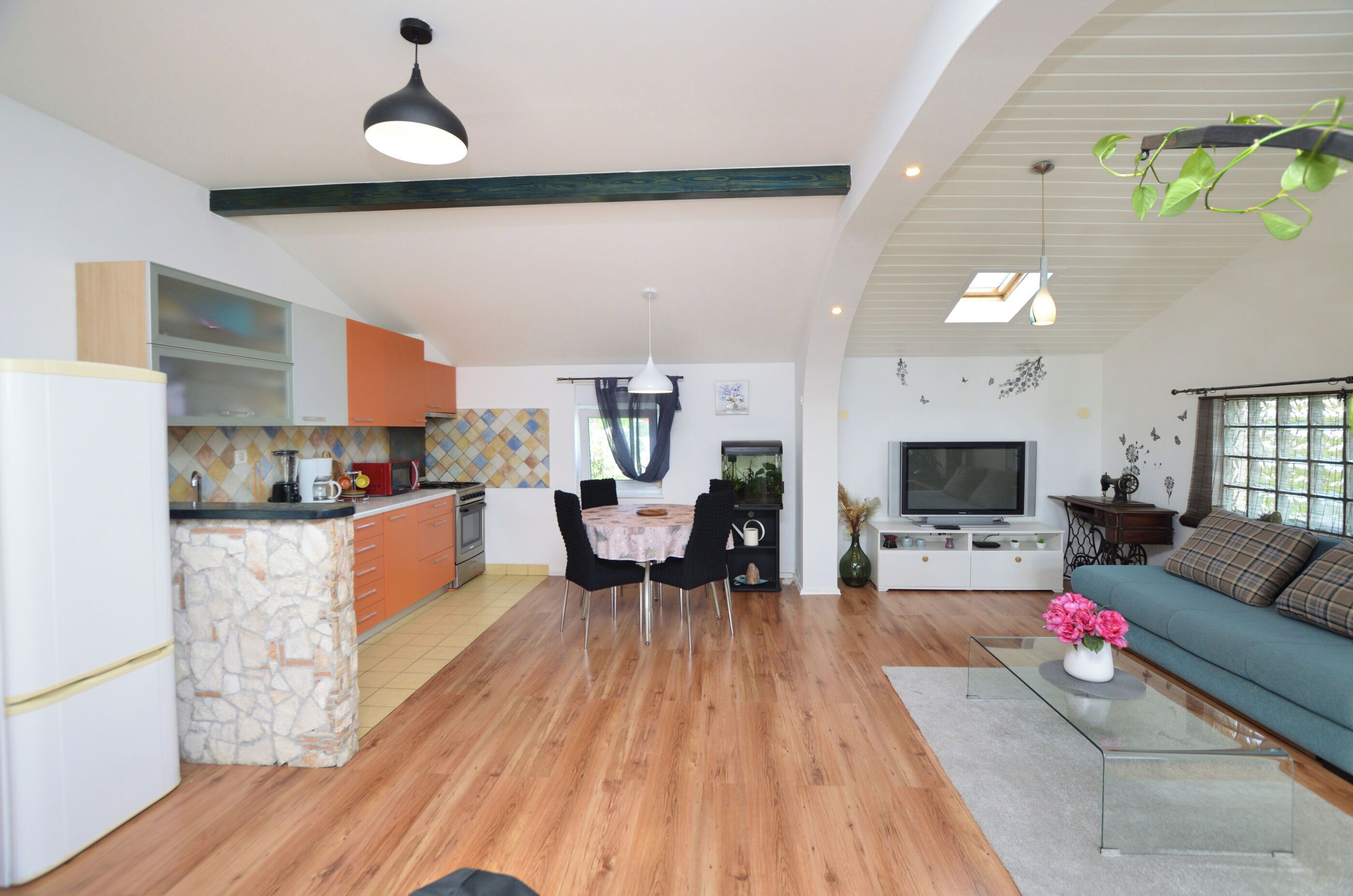 Eine moderne Küche mit einer Steinservierinsel, ein Essbereich mit rundem Tisch und ein Wohnzimmer mit Sofa und Fernseher.
