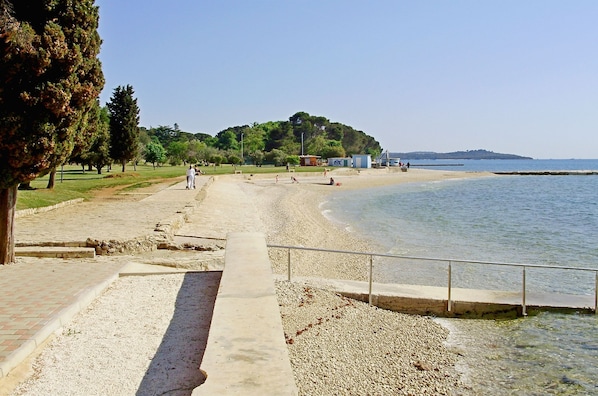 A beach with a pathway leading to the water, a small hill with trees, and a clear sky. - Apartment Emilija (Fazana)
