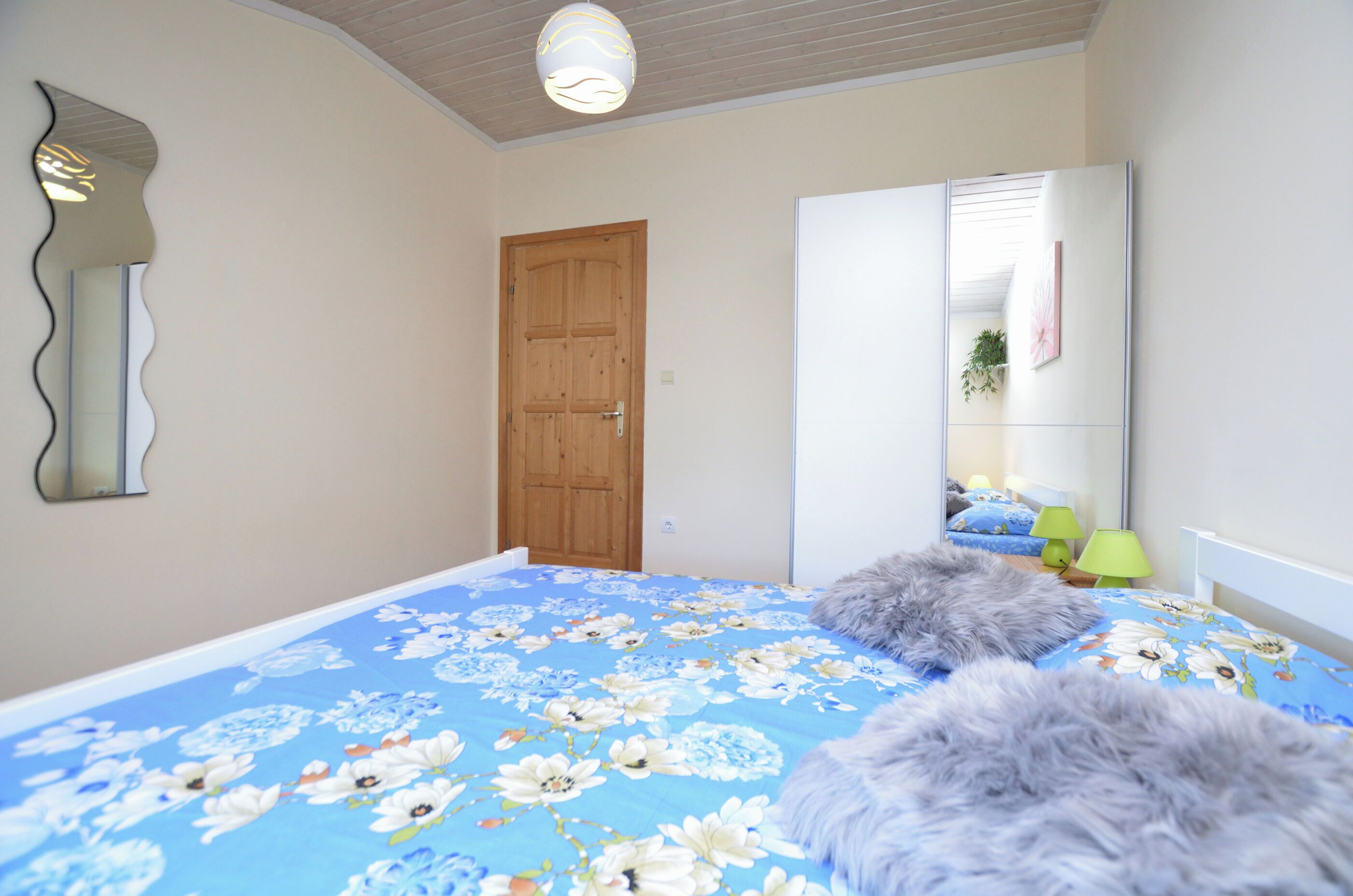 A bedroom with a floral bedspread, a wooden door, a mirror, and a green lamp.