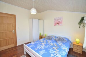 Ein Schlafzimmer mit Bett, Holzschrank, Nachttischlampe und einem Blumenbild an der Wand.