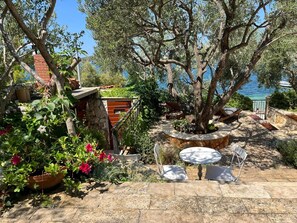 A garden with a stone bench, a small table, and a view of the sea. - Apartments Roza (Rogoznica)
