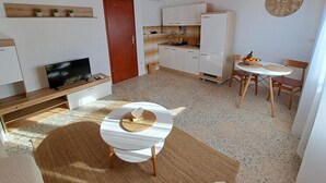 Egy kompakt, multifunkcionális lakótér, amelyben található egy kis konyhasarok, egy étkező egy kerek asztallal, egy televízió és egy kanapé.