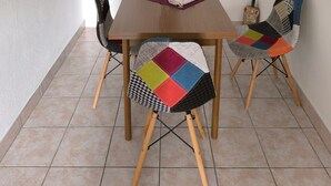 Un comedor con una mesa de madera, cuatro sillas con cojines de colores, un cuadro en la pared y una lámpara colgante.