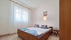 Un dormitorio con cama de madera, mesita de noche, lámpara de pared y ventana con cortinas translúcidas.